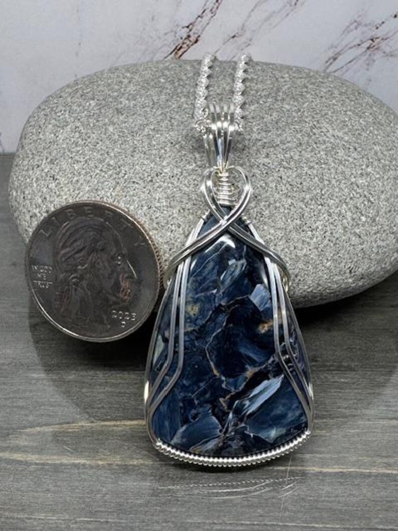 May include: A silver wire wrapped pendant featuring a blue and grey tiger's eye gemstone. The pendant is hanging from a silver chain.