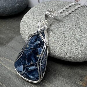May include: A silver wire wrapped pendant featuring a blue and black tiger's eye gemstone. The pendant is hanging from a silver chain.