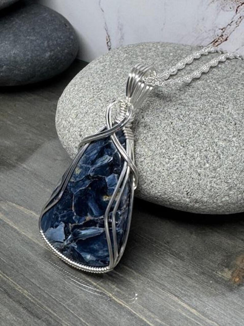 May include: A silver wire wrapped pendant featuring a blue and black tiger's eye gemstone. The pendant is hanging from a silver chain.