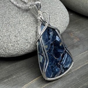 May include: A silver wire wrapped pendant featuring a blue and white tiger's eye gemstone. The pendant is hanging from a silver chain.