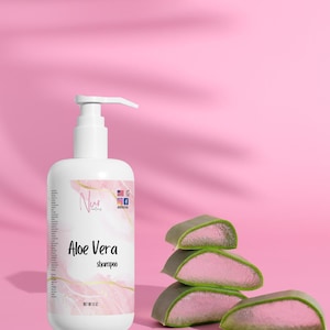 May include: White shampoo bottle with a pump dispenser, labeled "Aloe Vera shampoo." The bottle is next to a stack of aloe vera slices. The background is pink with a shadow.