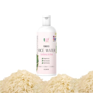 Op de afbeelding: Een witte plastic fles NUR Fermented Rice Water Conditioning Hair Rinse voor kroeshaar, kinky haar en krullen. De fles is gelabeld met de productnaam, ingredi&euml;nten en gebruiksaanwijzingen. De fles staat op een stapel witte rijst.