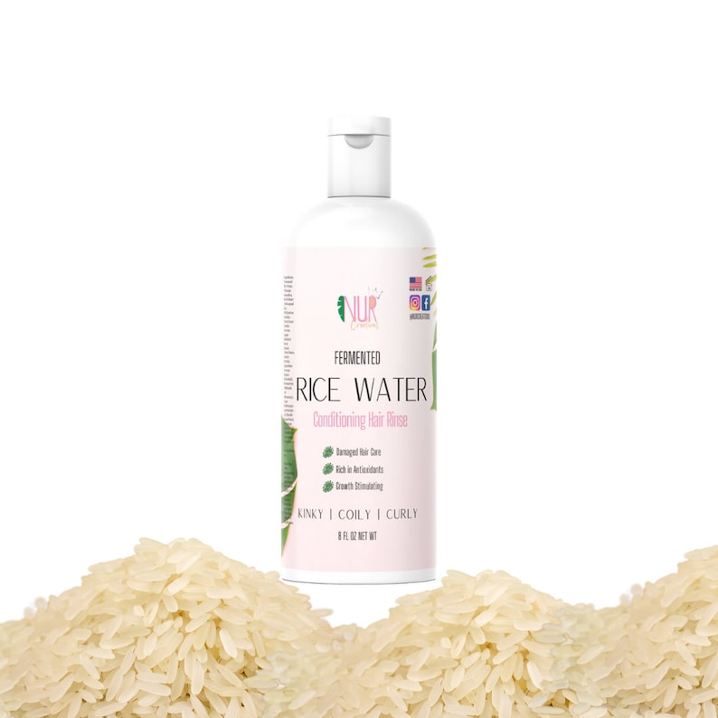 Op de afbeelding: Een witte plastic fles NUR Fermented Rice Water Conditioning Hair Rinse voor kroeshaar, kinky haar en krullen. De fles is gelabeld met de productnaam, ingredi&euml;nten en gebruiksaanwijzingen. De fles staat op een stapel witte rijst.