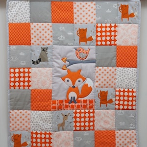May include: A patchwork quilt featuring a repeating pattern of orange, gray, and white squares. The quilt showcases appliqued foxes, birds, and other woodland creatures. The color palette includes orange, gray, and white, creating a cozy and inviting aesthetic.