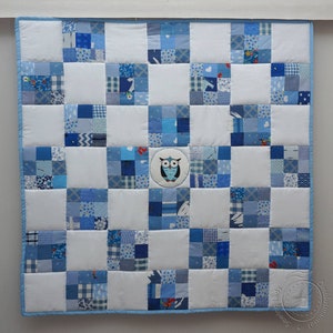 May include: A blue and white patchwork quilt with a white owl in a circle in the center. The quilt is made of many different squares of fabric, all in shades of blue.