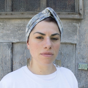 May include: A person wearing a blue and white patterned turban with silver hoop earrings and a nose ring. The person is wearing a white t-shirt.