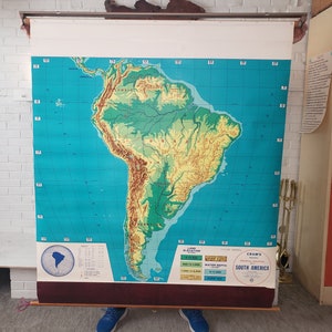 May include: A vintage, rolled-up map of South America with a blue background and green and yellow land elevations. The map is labeled "Cram's Physical Map of South America".