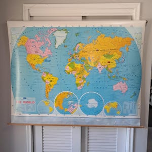 May include: A large, hanging political world map featuring colorful continents and oceans. The map displays the text THE WORLD and THE WORLD POLITICAL, with detailed borders, labels for countries, and circular polar projections at the bottom.