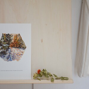 May include: A white print with a watercolor painting of a snowy forest path. The text "A winter breeze but warm sunlight" is at the bottom of the print.