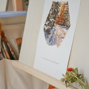 May include: A white framed print of a watercolor painting of a snowy forest path with the text "A winter breeze met with warm sunlight".