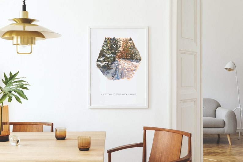 May include: A framed print of a painting depicting a snowy forest path with the text "A winter breeze met warm sunlight". The print is hanging on a white wall in a room with a wooden table and chairs.