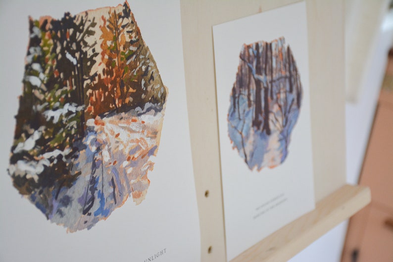 May include: Two watercolor paintings of winter scenes. The first painting shows a snowy path through a forest with trees on either side. The second painting shows a similar scene, but with a more blue color palette. Both paintings have a rough, textured edge.