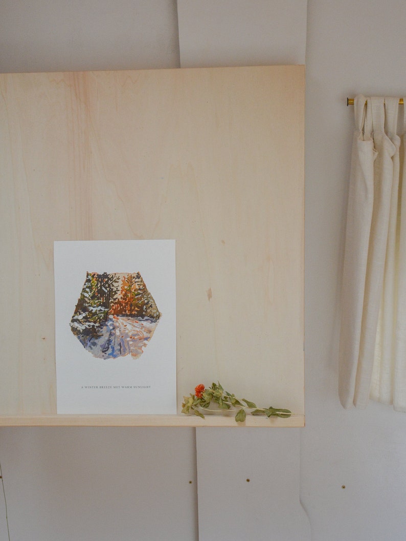 May include: A white framed print with a painting of a snowy forest path. The text "A winter breeze, yet warm sunlight" is at the bottom of the print.