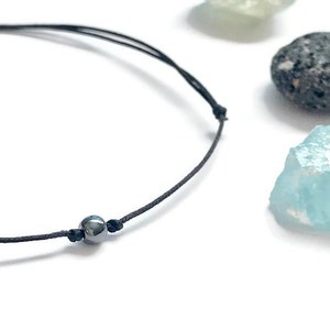 Puede incluir: Un brazalete simple de cuerda negra con una sola cuenta negra.