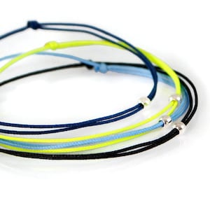 May include: A set of four bracelets made with thin cords in black, blue, light blue, and neon yellow. The bracelets are tied together with silver beads.