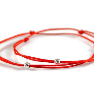 Pode incluir: Pulseira de cordão vermelho com duas contas prateadas.