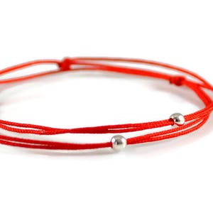 Könnte beinhalten: Rotes Armband mit zwei silbernen Perlen.