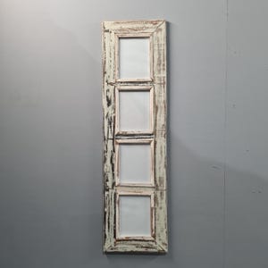 Può includere: Una cornice verticale e rettangolare da parete con quattro aperture. La cornice ha una finitura bianco sporco anticata con venature del legno visibili e accenti marrone scuro. Ogni apertura è quadrata.