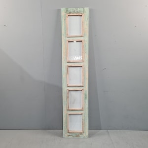 May include: A vertical, rectangular, distressed wooden frame with five square openings. The frame is painted in a faded, light green colour with pink accents around the openings. The openings appear to be for photos or artwork.