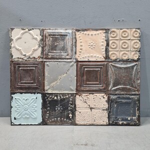 May include: A rectangular wall art piece composed of twelve square metal tiles. The tiles feature various embossed patterns and textures, with a distressed, aged appearance. Colors include off-white, brown, gray, and pale blue.
