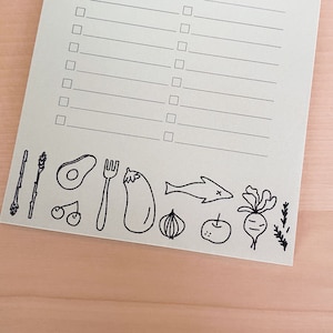 Op de afbeelding: Een checklist met een lege ruimte om te schrijven en een rij zwart-wit illustraties van verschillende voedingsmiddelen, waaronder een avocado, een vork, een aubergine, een ui, een appel, een vis, een radijs en takjes rozemarijn.