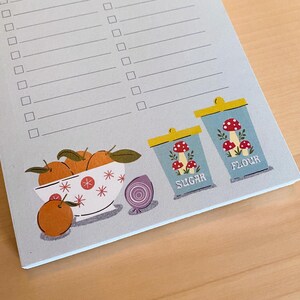 May include: A blue and white notepad with a checklist and a decorative illustration of a bowl of oranges, an onion, and two blue and white canisters labelled "Sugar" and "Flour".