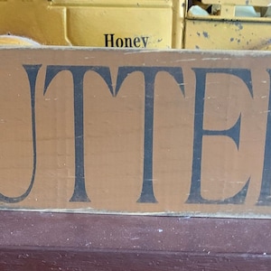 May include: A brown wooden sign with the word "BUTTERY" painted in black letters.