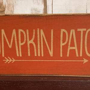 May include: Wooden sign with an orange background and the words "PUMPKIN PATCH" in white, with an arrow pointing right. The sign has a rustic, distressed look, perfect for fall decor.