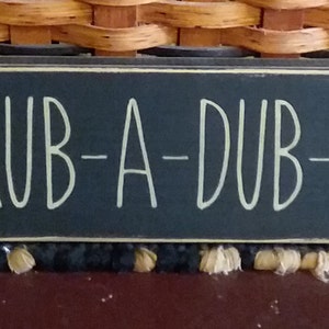 May include: A black wooden sign with white lettering that reads "SCRUB-A-DUB-DUB".