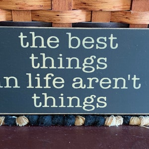 May include: A black wooden sign with white text that reads "the best things in life aren't things".