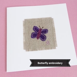 A handmade card featuring a purple butterfly embroidered on a piece of linen fabric. The card is white.