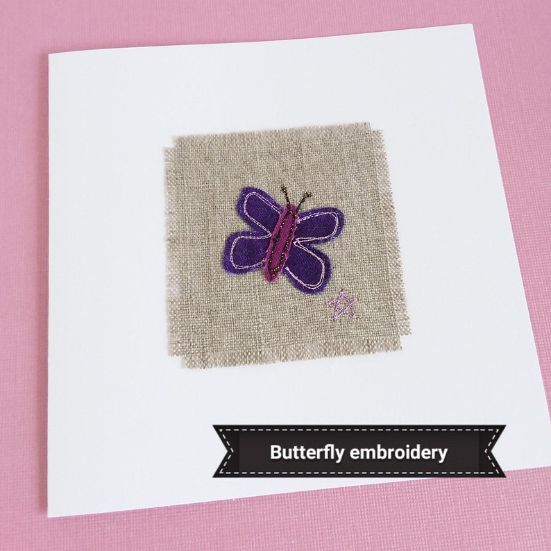 A handmade card featuring a purple butterfly embroidered on a piece of linen fabric. The card is white.