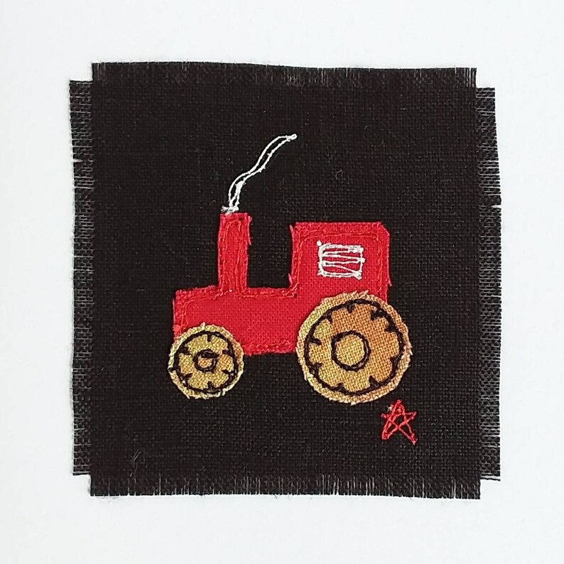 Puede incluir: Un tractor rojo bordado con ruedas amarillas sobre un fondo de tela negro. Una peque&ntilde;a estrella roja est&aacute; bordada debajo del tractor.