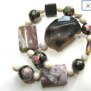 May include: A brown and white agate stone pendant with a black and white floral design on the beads. The beads are strung on a white cord.
