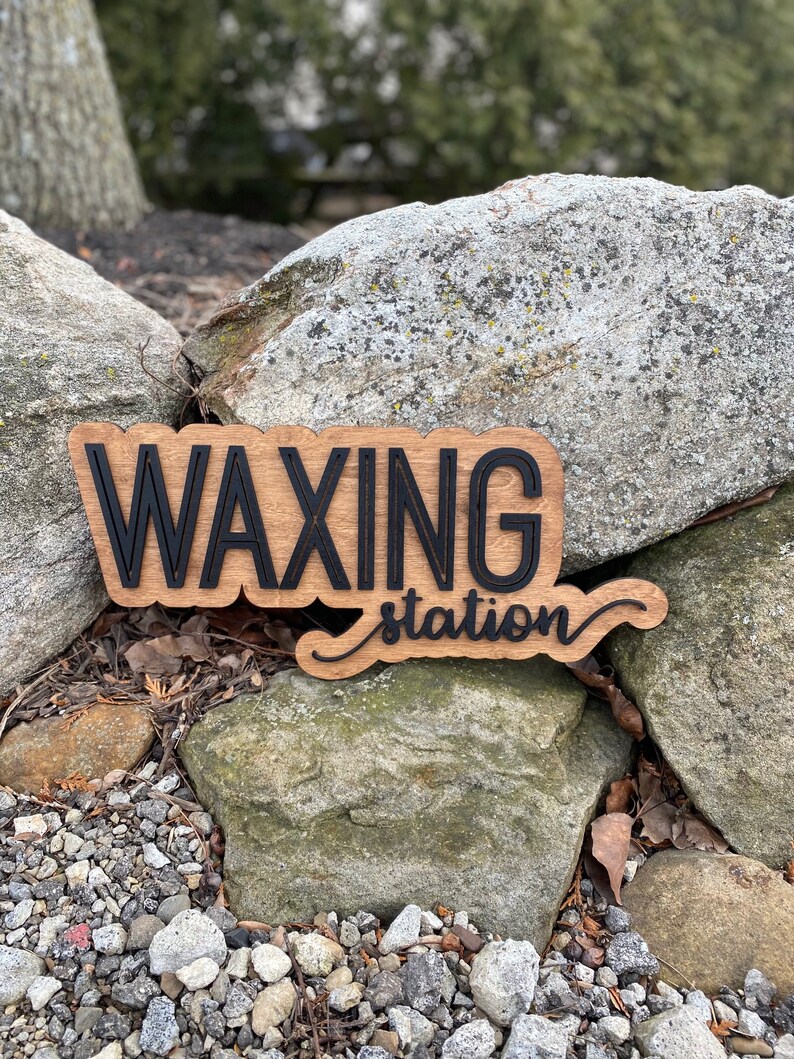 May include: A wooden sign with the words "Waxing Station" in black lettering. The sign is sitting on a pile of rocks.