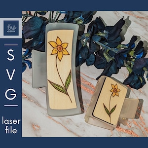 May include: Two wooden hair clips with a light wood background and a yellow flower design. The clips are translucent and have a light blue tint.