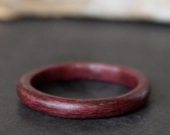May include: A close-up of a dark purple wooden ring. The ring is smooth and polished, and it has a simple, elegant design.