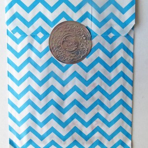 May include: A blue and white chevron patterned paper bag with a silver circular sticker. The sticker has a decorative design.