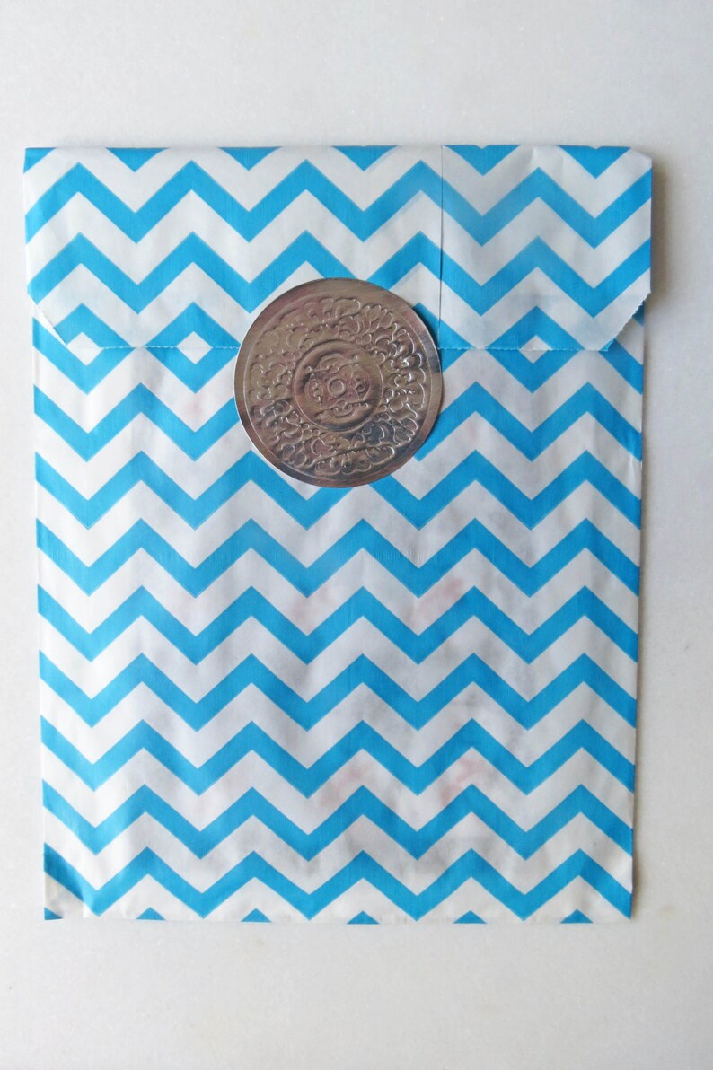 May include: A blue and white chevron patterned paper bag with a silver circular sticker. The sticker has a decorative design.