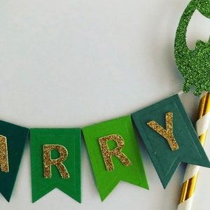 May include: Green and gold glitter cake topper with the word "Happy" spelled out on a banner.