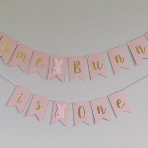 Op de afbeelding: Roze en gouden banner met de tekst "Some bunny is one". De banner is gemaakt van vilt en heeft aan elke kant een konijnensnijding.