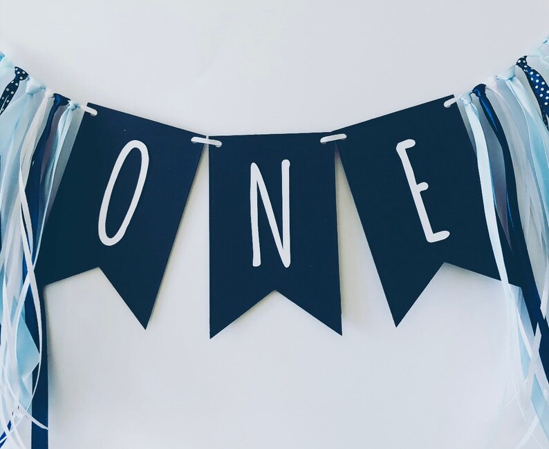 Puede incluir: Una pancarta negra y blanca con la palabra "ONE" en letras blancas. La pancarta est&aacute; decorada con cintas azules y blancas.