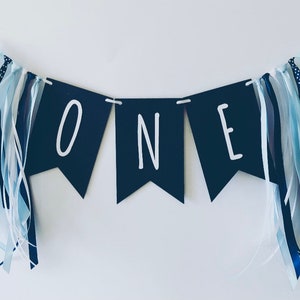 Puede incluir: Una pancarta azul marino con letras blancas que deletrean "ONE" con cintas azules y blancas.