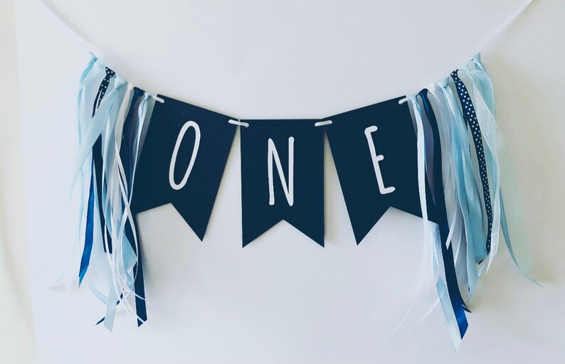 Puede incluir: Una pancarta azul marino con letras blancas que deletrean "ONE" con cintas azules y blancas.