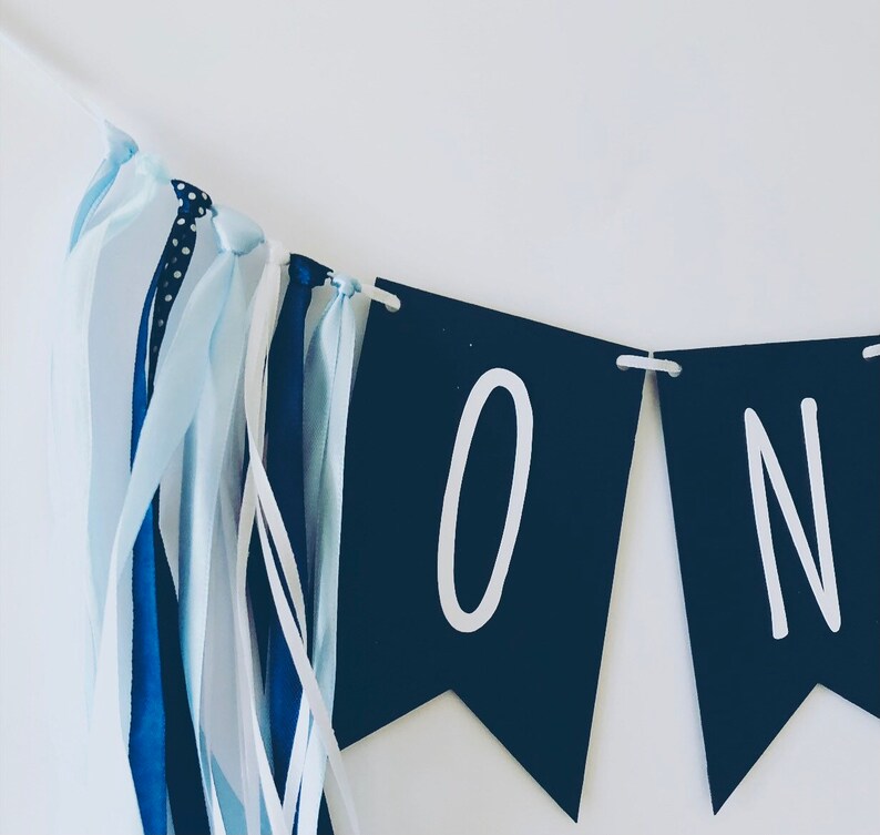 Puede incluir: Una pancarta azul y blanca con la palabra "ONE" en letras blancas sobre banderines negros. La pancarta tiene cintas azules y blancas.