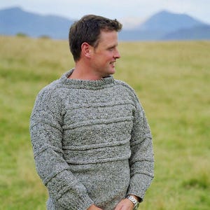 May include: A gray knitted sweater with a textured pattern. The sweater has a crew neck and long sleeves.