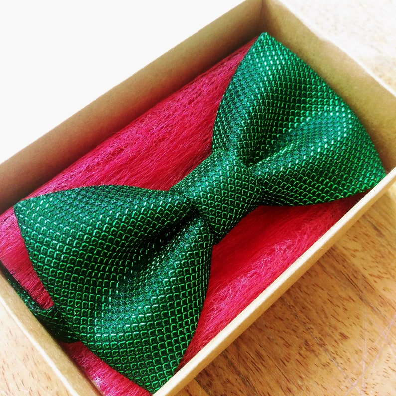 May include: A green bow tie with a sparkly, textured finish, displayed in a box with red tissue paper.