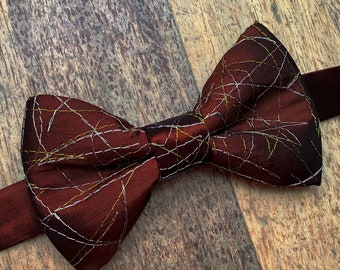 Red bow tie with white and gold lines, shimmering satin texture