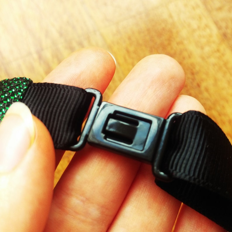 May include: A black adjustable strap with a plastic buckle. The strap is made of a woven fabric and has a smooth finish.