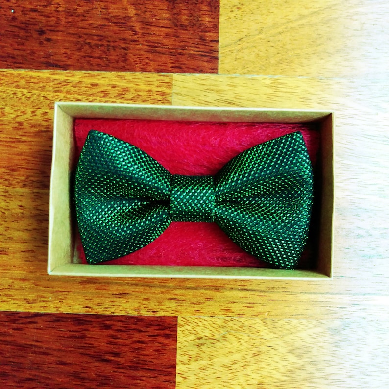 May include: A green bow tie with a textured pattern, displayed in a brown box with red lining.